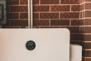 Witte thuisbatterij met groen laadlampje aan een bakstenen muur